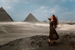 Young redhead tourist girl wearing a brown dress standing on the sand in Egypt, Cairo - Giza. Pyramids on backround. Copy space