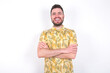 © Jihan - Young caucasian man wearing Hawaiian t-shirt over white background  being happy smiling and crossed arms looking confident at the camera. Positive and confident person.