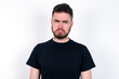 © Jihan - young caucasian bearded man wearing black t-shirt standing over white wall depressed and worry for distress, crying angry and afraid. Sad expression.