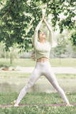 Fototapeta Las - A young beautiful slender girl with long blonde hair does yoga in the summer in nature by the pond in the park.