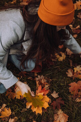 Young woman collecting colorful maple leaves from the ground into bunch