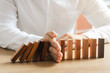 © Thapana_Studio - Risk management, business man hand Stop the continuous falling of wooden dominoes, stop the impact of the business crisis. hedging Solving business problems for success.