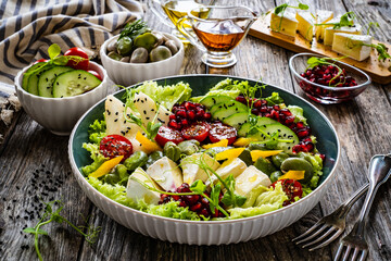 Poster - Tasty salad - leafy greens, camembert, pear,  pomegranate, cherry tomatoes and broad bean on wooden table
