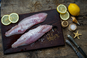 Wall Mural - two fresh clean fish fillets on a board with lemons and spices