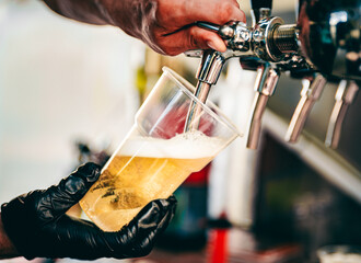 hand at beer tap pouring a draught beer in plastic glass serving in a cafe