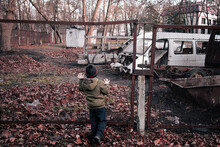 A Little Boy Looks At A Junkyard Of Broken Cars. The Kid Next To The Car Graveyard