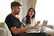 © saltdium - Young Asian couple  sitting on sofa together while a man looking on laptop, Domestic life and Domestic home concept.