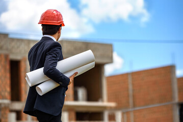 man engineer architect in red helmet is holding a paper plan of a building at the construction site and verifying the working process..