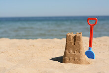 Sand Castle And Child Plastic Shovel On Beach Near Sea. Space For Text