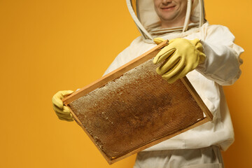 Wall Mural - Beekeeper in uniform holding hive frame with honeycomb on yellow background, closeup