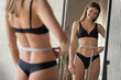 Reflection in mirror of slim fit woman measuring waist after dieting and workout marathon