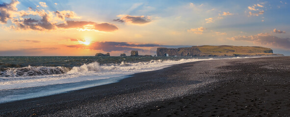 Picturesque autumn sunset Dyrholaey Cape and  rock formations view from Reynisfjara ocean black volcanic sand beach. Vik, South Iceland.