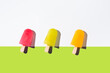 Paletas de hielo de colores. Palitos de helado naranja, rojo y amarillo sobre fondo verde y blanco. Concepto de verano. Vista superior