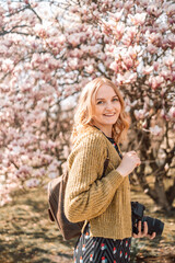 Fashion style beauty romantic portrait of young pretty beautiful 30s woman with long blonde hair posing between pink magnolia. Stunning girl looking at you or in camera. 