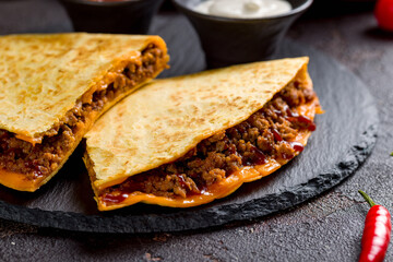 Wall Mural - Quesadilla with beef, cheese, bbq sauce and sauces on dark stone plate macro close up