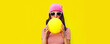 Fashionable portrait of stylish cool young woman inflating chewing gum wearing pink hat on yellow background