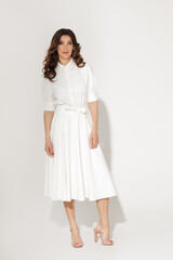 Self confident brunette women in white dress with wavy hair and natural fresh make-up posing on a white background. Spring or summer elegant fashion concept