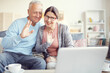 © Mediaphotos - Cheerful modern grandparents sitting on sofa and waving hands to laptop webcam while communicating online