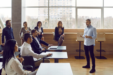 Successful male presenter or coach lead team business meeting or conference with employees in office. Businessman or man speaker talk in front of employee at team seminar at company briefing.