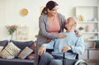 © Mediaphotos - Happy attractive senior woman with ponytail touching shoulders of her husband in wheelchair while chatting with him in living room