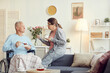© Mediaphotos - Serious attractive senior woman with ponytail sitting on elbow of sofa and gesturing hand while sharing news with husband in wheelchair