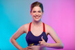 Sporty happy young woman in sports bra wear with thumb up. Female fitness portrait isolated on neon color background. Healthy lifestyle concept with yoga instructor.