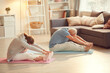 © Mediaphotos - Senior couple in sportswear sitting on exercise mats in living room and bending forward while stretching backs with yoga