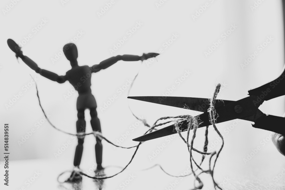 Wooden puppet tied with ropes to the puppeteer and scissors cut the rope, manipulation of people and freedom, strength and freedom