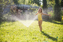 Happy Child Girl Playing With Garden Hose And Having Fun With Spray Of Water In Sunny Backyard. Summer Time. Kid Boy Helps Water Garden With Hose. Slow Life. Enjoying The Little Things. Summer Holiday