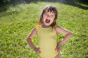 Happy child girl playing with garden hose and having fun with spray of water in sunny backyard. Summer time. Kid Boy helps water garden with hose. Slow life. Enjoying the little things. Summer holiday