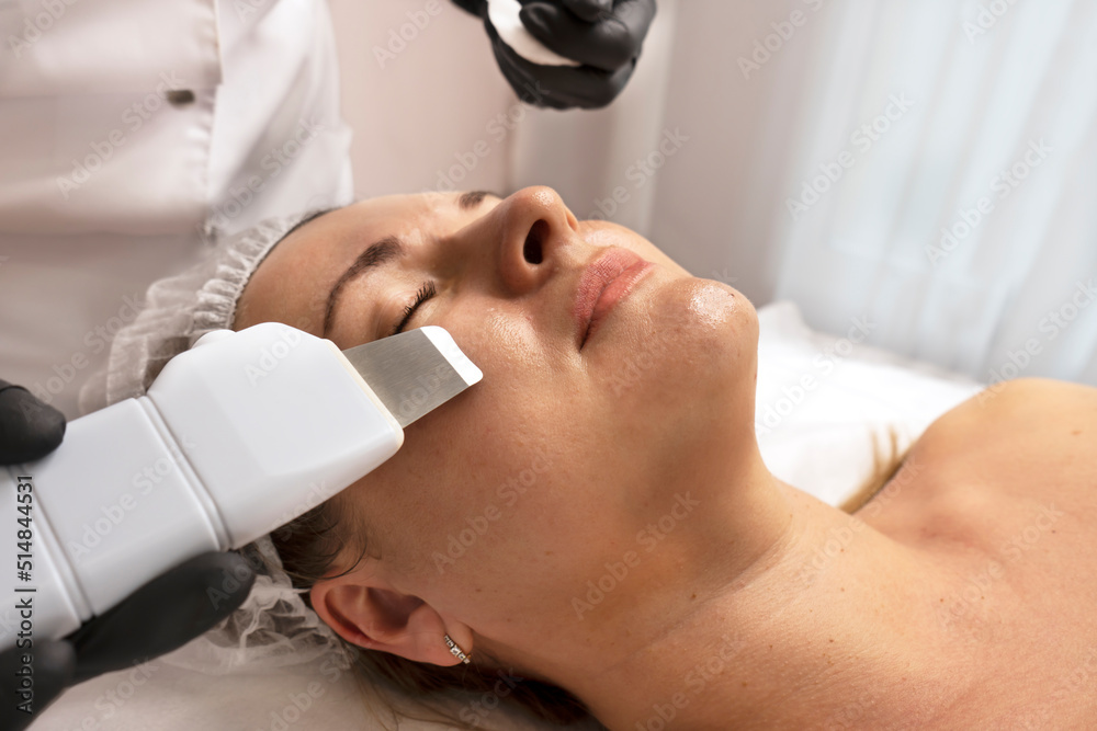 Procedure with ultrasonic skin scrubber. Woman face scrubber treatment with ultrasonic spatula. Facial pore comedones blackheads cleansing tool. Stock Photo Adobe Stock