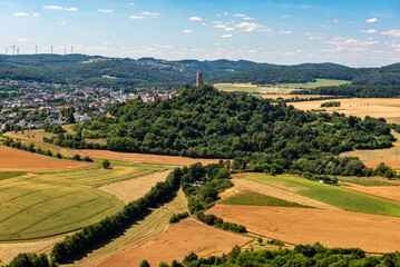 Der Bergfried der Höhenburg Vetzberg auf einem Vulkanberg in Mittelhessen, eingebettet in eine landwirtschaftlich genutzte Landschaft mit leicht bewölktem Himmel am Horizont bei schönem Sommerwetter