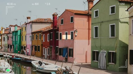 Wall Mural - Burano, Venice, Italy - July 2, 2022: A look through the photo camera at brightly colored houses and water canal with boats in Burano, people walk and rest on streets