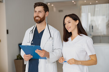 Wall Mural - Portrait of happy doctor and nurse standing near reception in hospital and looking away
