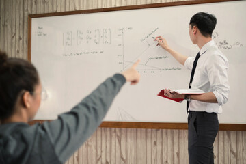 an asian male teacher in a classroom near the whiteboard is writing and teaching a lesson with a spe