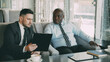 © silverkblack - Two multi-ethnic businessmen looking at clipboard and discussing startup projects in modern cafe during lunch time