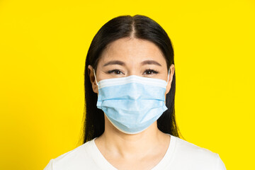 Happy, safe of pandemic mature asian woman wearing medical face mask coronavirus or monkeypox prevention. Charming middle age woman in white t-shirt and medical mask on yellow background