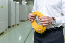Businessman Holding Rolled Yellow Cables In Factory