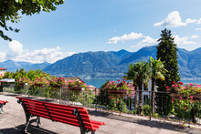 Switzerland, Ticino, Locarno, Park Bench Overlooking Lake Maggiore And Surrounding Mountains In Summer