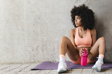 Thoughtful Woman With Water Bottle Sitting On Exercise Mat