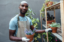 Smiling Bald Man Holding Potted Plants Standing In Garden