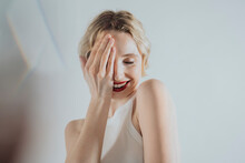 Shy Woman Covering Eye With Hand Against White Background
