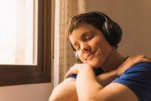Smiling Woman With Eyes Closed Listening Music Through Wireless Headphones At Home
