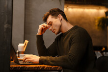 Young White Man Thinking And Looking Tired While Using Laptop In Cafe