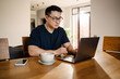 Adult calm asian man in glasses working with laptop