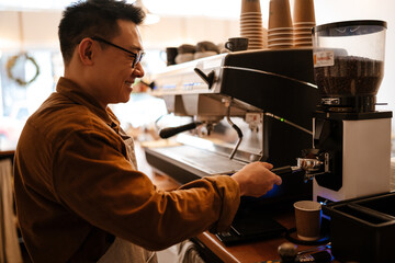 Wall Mural - Adult asian man making coffee with machine while working in cafe