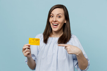 Young happy surprised shocked amzed fun woman she 20s wears casual blouse hold in hand point index finger on mock up of credit bank card isolated on pastel plain light blue background studio portrait