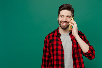 Wall Mural - Young happy smiling fun caucasian man he 20s wearing red shirt grey t-shirt talk speak on mobile cell phone conducting pleasant conversation isolated on plain dark green background studio portrait
