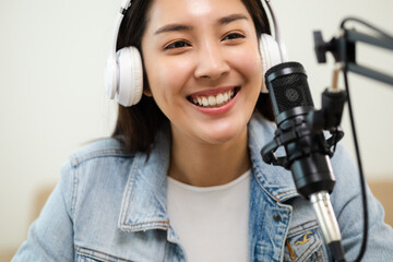 Wall Mural - Content creator woman host streaming her a podcast on laptop with headphones and microphone interview cheering guest conversation at broadcast studio. Blogger motivation recording voice over radio.