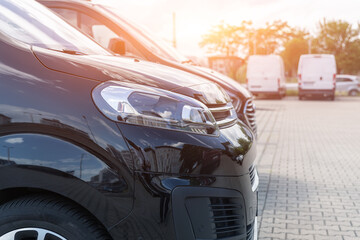 Wall Mural - Close-up detail headlight view of many modern luxury black vans parked in row at car sale rental leasing dealer against sunset. Commericial trasfer cargo transportation company fleet. Vip charter